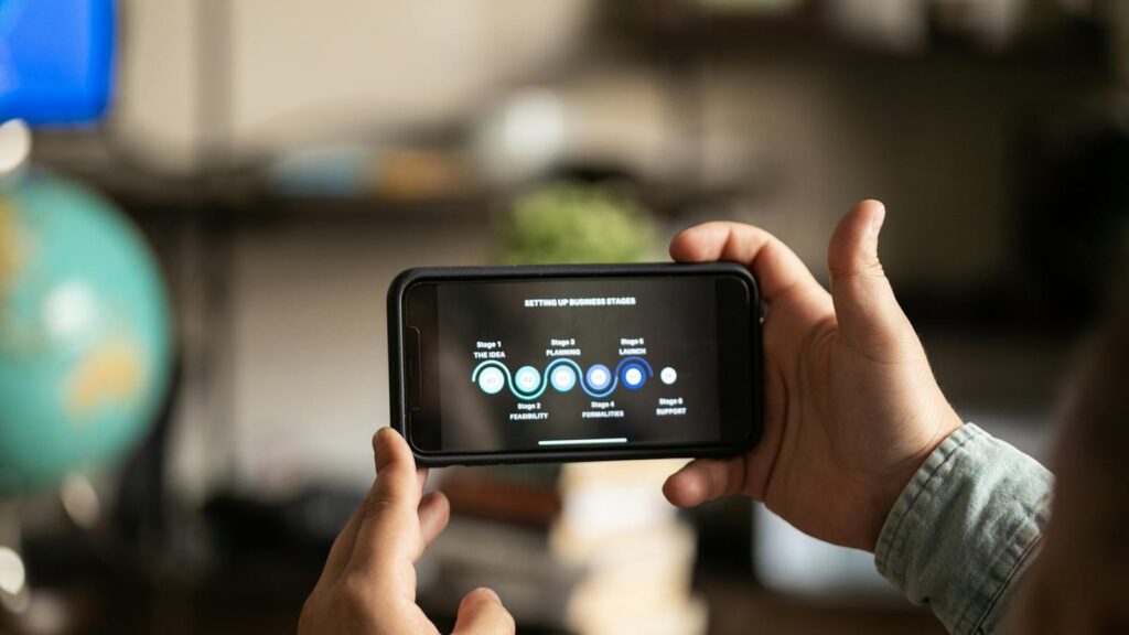 App-Entwicklung: Hände halten ein Smartphone, auf dem Bildschirm mehrere Business-Schritte. Heimliche Umgebung.